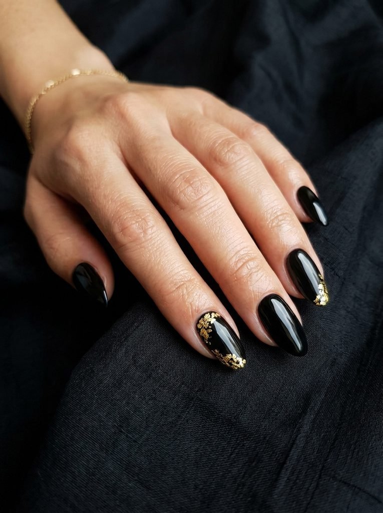 alt="Glossy jet black nails with delicate gold leafing accents - luxury black Halloween nails"